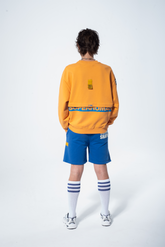 Model in the Haresquare Superhuman Apricot Tan sweatshirt with Blue print, styled with Haresquare Blue shorts – unisex luxury streetwear from Ireland.
